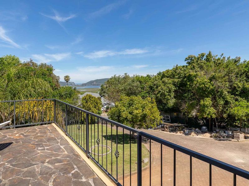 An elevated balcony featuring stone paving and a metal balustrade, offering scenic views of the surrounding landscape and garden area.
