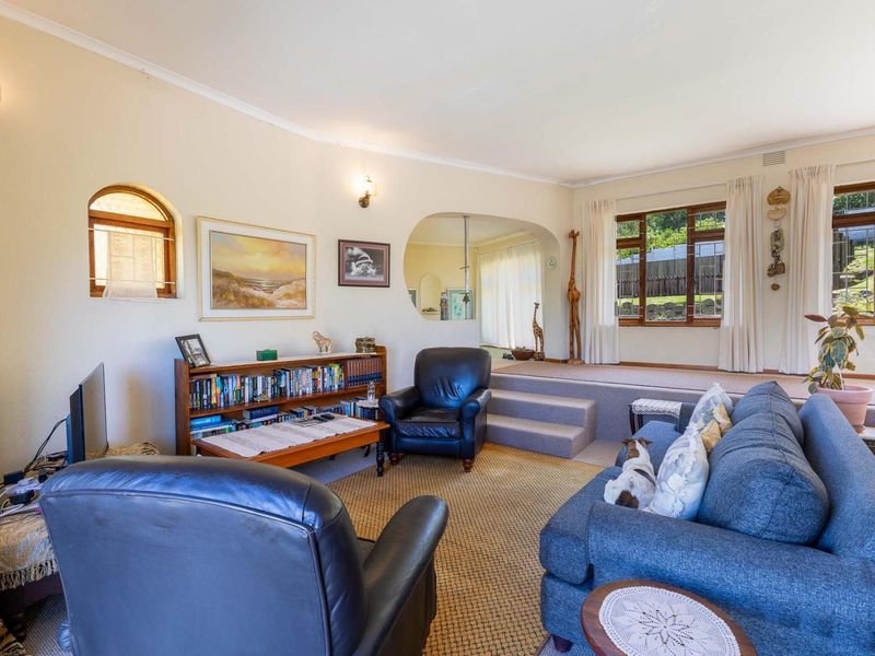 A spacious sunken living room featuring arched architectural detailing, carpeted flooring, and large windows that provide natural light and garden views.