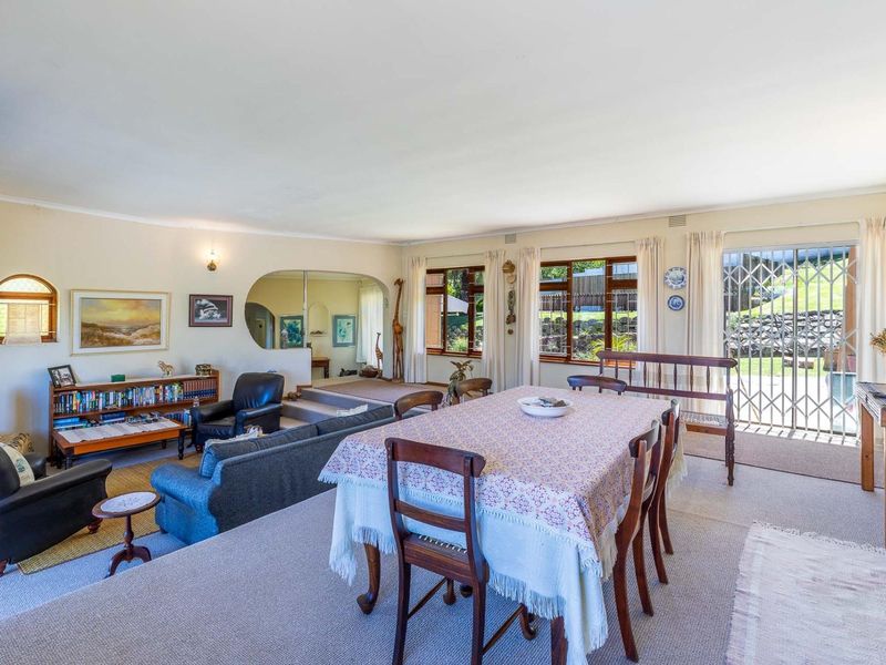 Spacious open-plan living and dining area featuring large windows, an arched transition to an adjacent space, and direct access to the garden via a security gate.