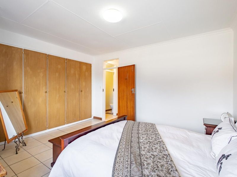 A bedroom featuring tiled flooring, built-in wooden cupboards, and direct access to an en-suite bathroom.