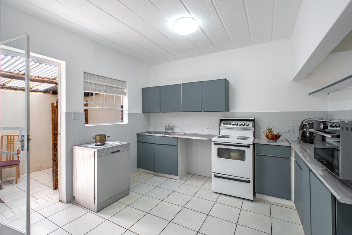 Functional kitchen featuring grey cabinetry, tiled backsplash, tiled flooring, and a freestanding stove, with direct access to an outdoor area.
