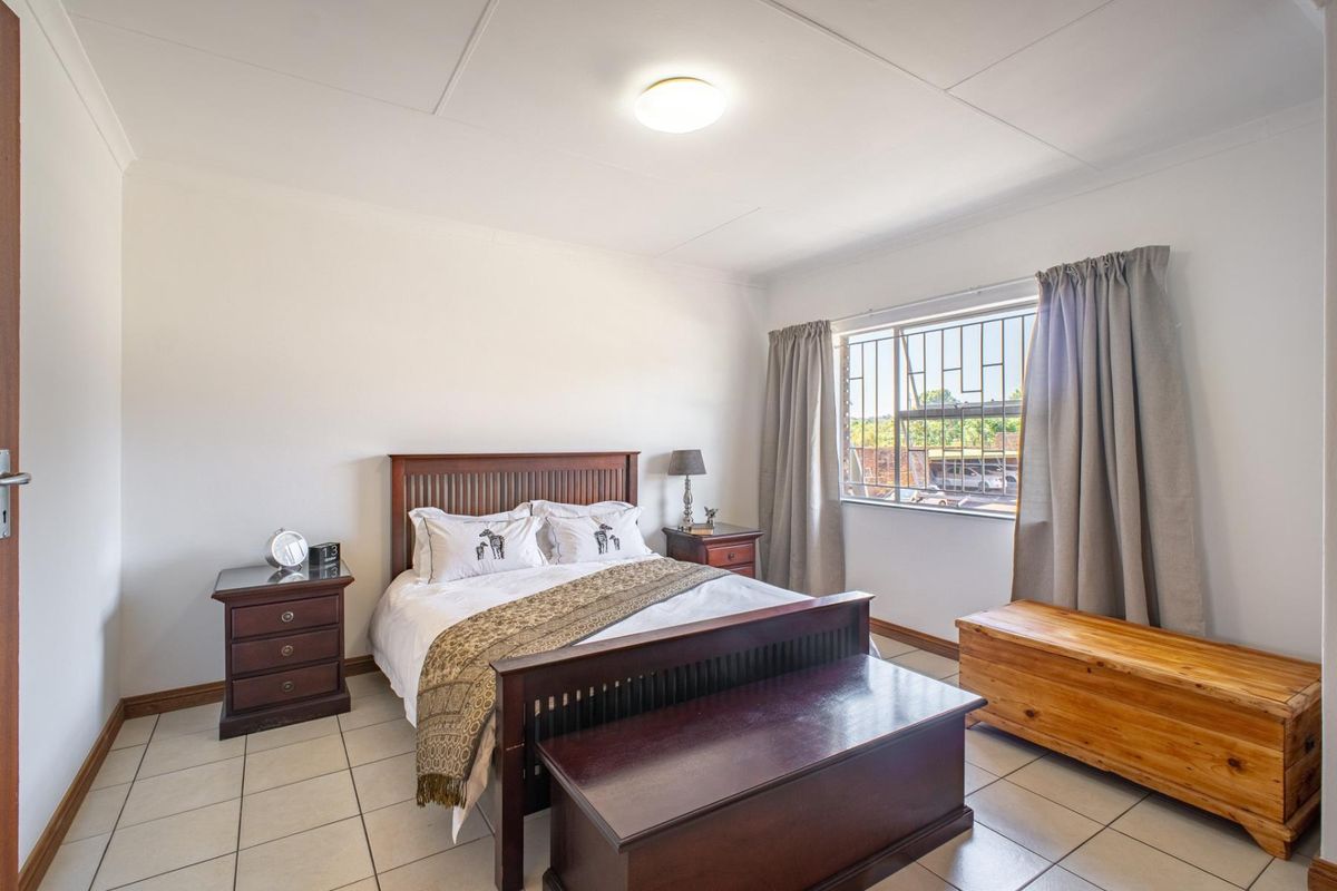A well-lit bedroom featuring tiled flooring, a window with security bars, and a neutral color palette, offering a functional and comfortable living space.