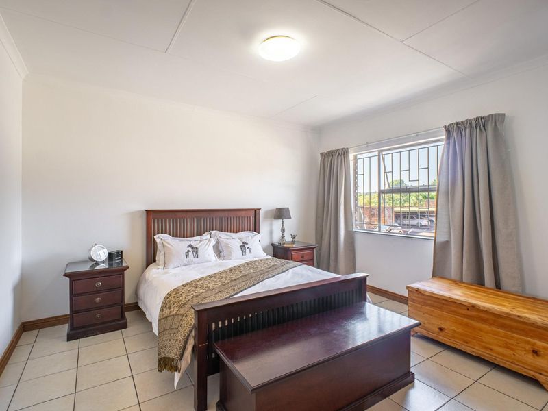 A well-lit bedroom featuring tiled flooring, a window with security bars, and a neutral color palette, offering a functional and comfortable living space.