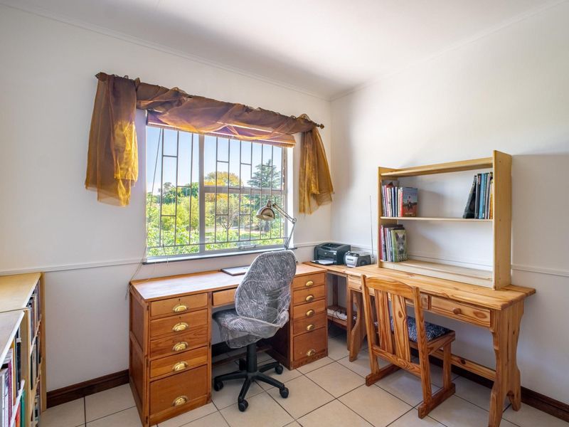 A functional home office space featuring tiled flooring, a chair rail, and a window fitted with security bars.