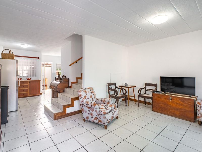 Open-plan living area featuring tiled flooring, a central staircase with a wooden handrail, and an integrated kitchen space with built-in cabinetry.