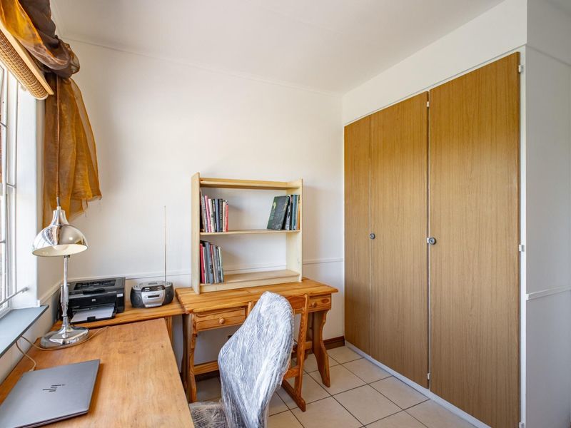 A functional bedroom featuring tiled flooring and built-in wooden cupboards, currently utilized as a home office space.