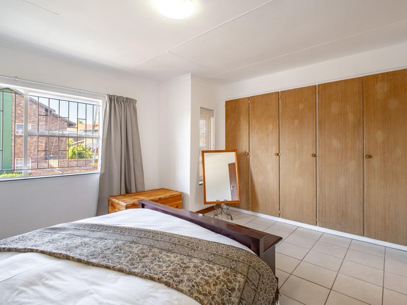 A bedroom featuring tiled flooring, built-in wooden cupboards, and a window with security bars, offering a functional space with potential for modernization.