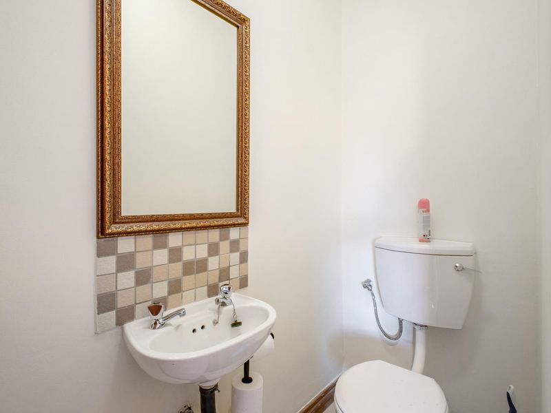 A compact guest bathroom featuring a wall-mounted basin with a tiled splashback, a toilet, and a decorative wall mirror.