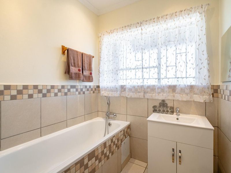 A functional bathroom featuring a bathtub, vanity cabinet with basin, and neutral wall tiling with decorative mosaic accents.