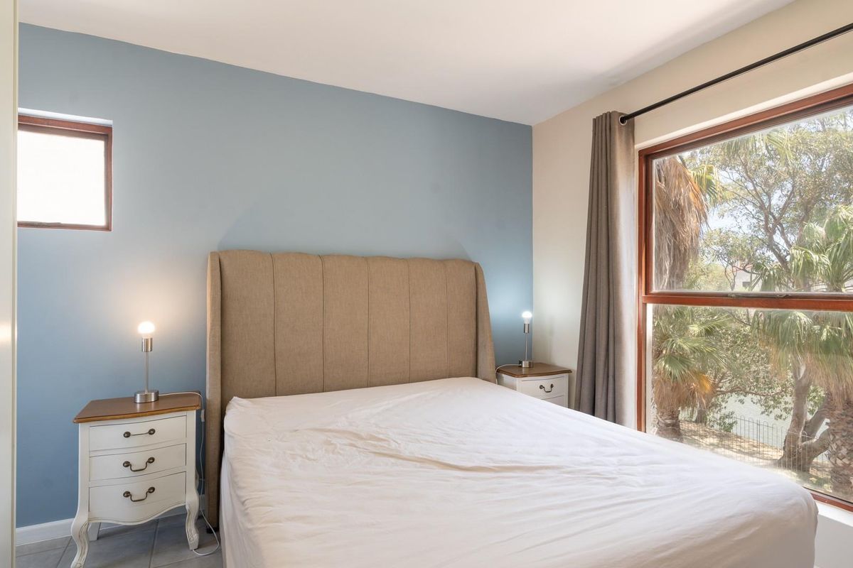 A bright bedroom featuring a blue accent wall, built-in wardrobe, and large windows providing natural light and garden views.