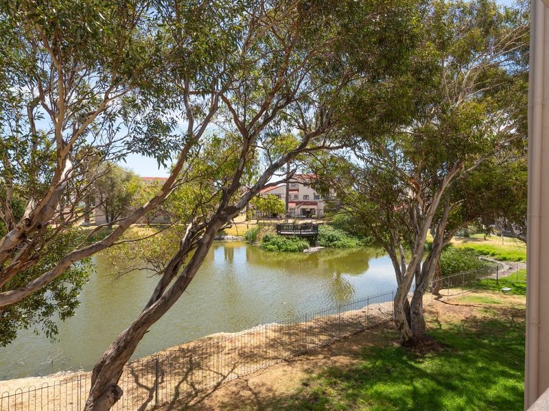 A scenic view overlooking a tranquil pond and landscaped grounds, framed by mature trees from the perspective of a balcony.