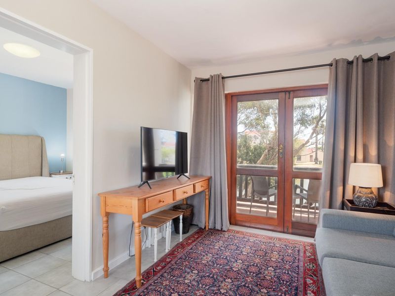 Living area featuring tiled flooring and timber-framed glass doors leading to an outdoor space, with an adjacent bedroom visible through the doorway.