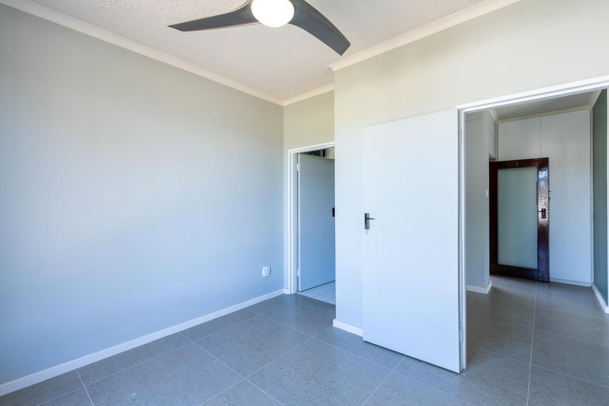 An empty bedroom featuring neutral wall paint, tiled flooring, and a modern ceiling fan, providing a clean and versatile space.