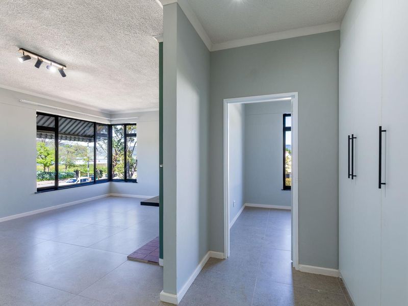 A bright, empty hallway featuring tiled flooring, built-in storage cupboards, and a view into the adjacent living area with large windows.