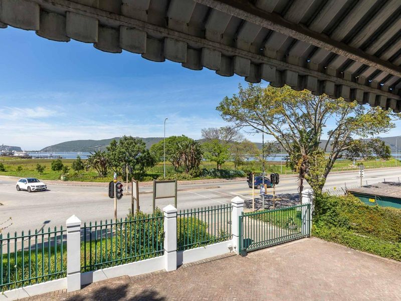 Covered balcony area featuring paved flooring and metal fencing, offering an elevated view of the surrounding street and landscape.
