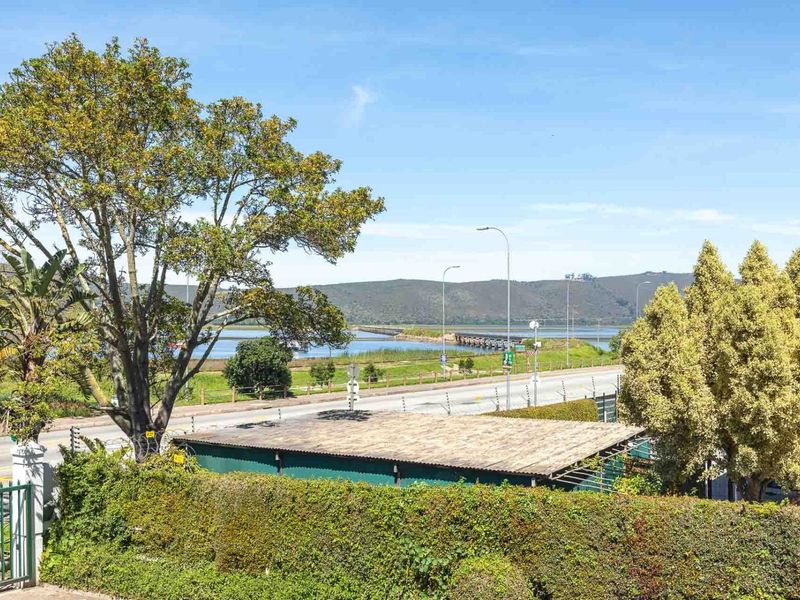 An elevated outdoor view overlooking a road, bridge, and scenic landscape with mature trees and established hedging.