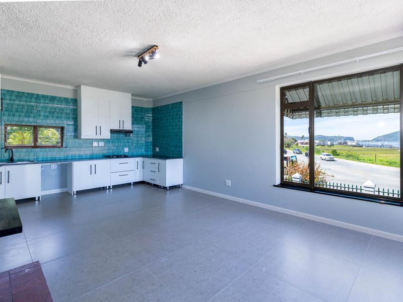 An open-plan living and kitchen area featuring modern white cabinetry, vibrant blue tiled backsplash, and large windows with scenic views.
