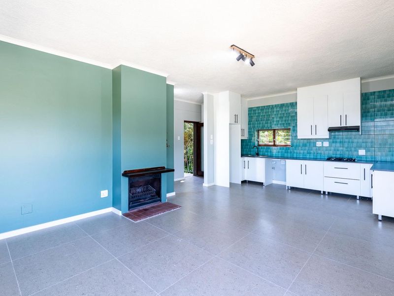 Spacious open-plan living area featuring a built-in fireplace and a modern kitchen with white cabinetry and vibrant blue tiled backsplash.