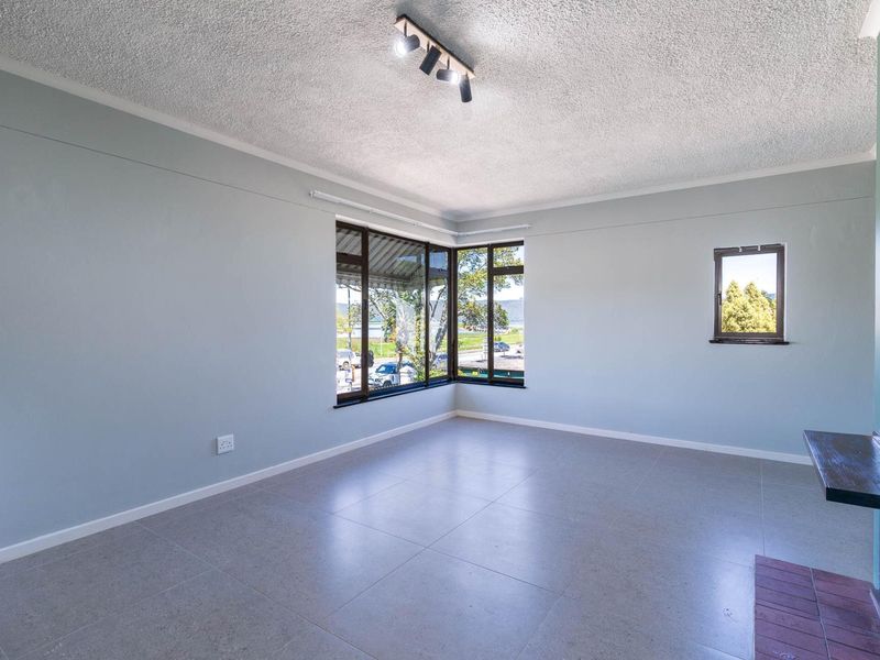 An empty living room featuring tiled flooring, a popcorn ceiling, corner windows with natural light, and a built-in fireplace hearth.