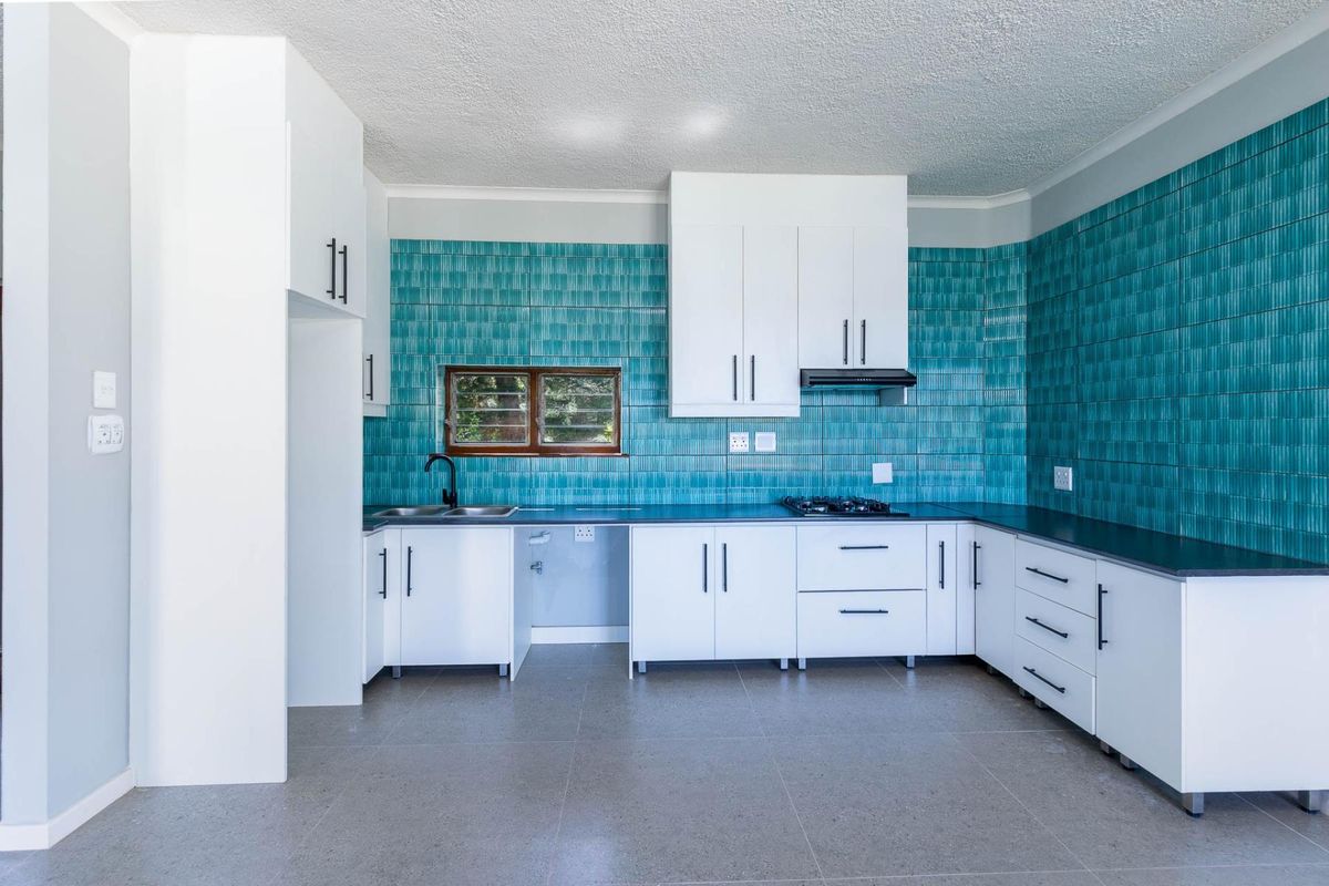 A modern, clean kitchen featuring white cabinetry, a striking teal tiled backsplash, gas hob, extractor fan, and durable tiled flooring.