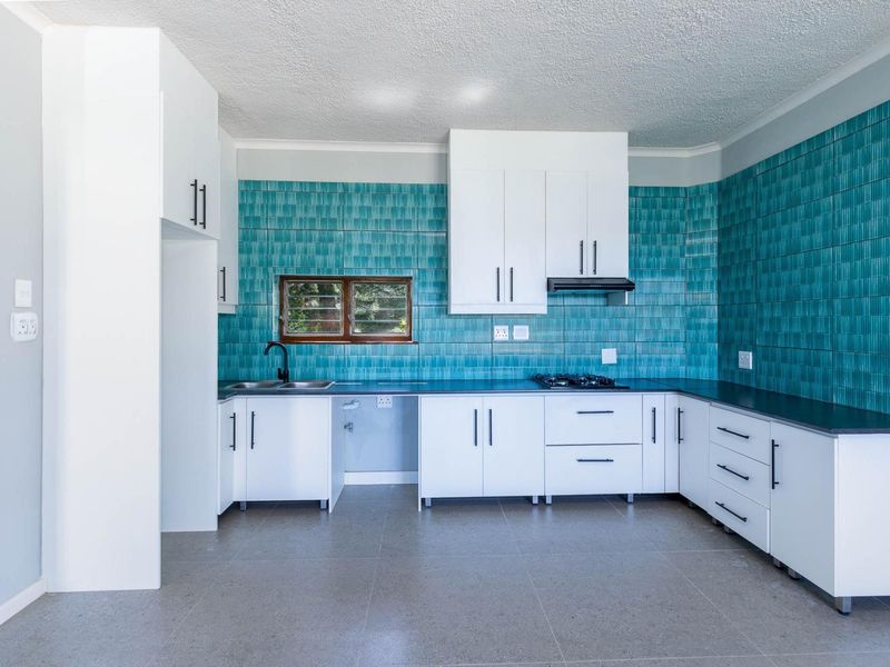 A modern, clean kitchen featuring white cabinetry, a striking teal tiled backsplash, gas hob, extractor fan, and durable tiled flooring.