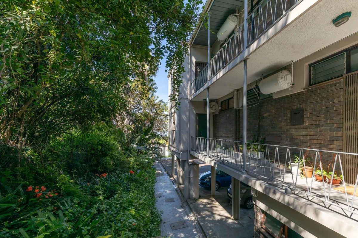 Rear exterior view of the apartment building featuring a brick facade, metal balcony railings, and an adjacent landscaped garden area.