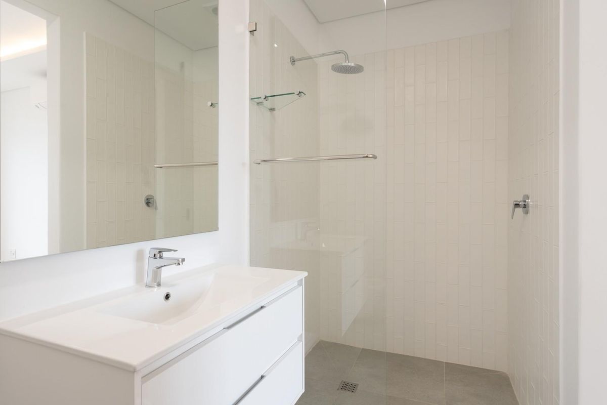 Modern bathroom featuring a sleek vanity with integrated basin, large wall mirror, and a spacious walk-in shower with glass screen and rain shower head.