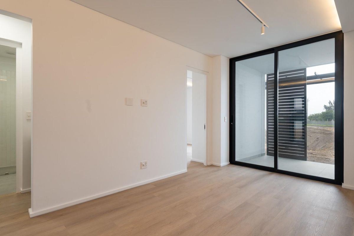 A bright, modern bedroom featuring light laminate flooring, recessed lighting, and a large sliding glass door leading to an outdoor area.