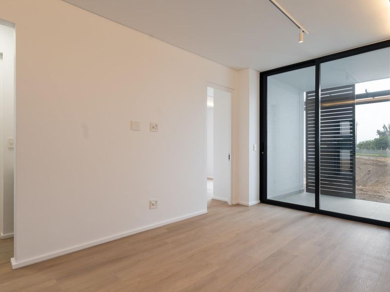 A bright, modern bedroom featuring light laminate flooring, recessed lighting, and a large sliding glass door leading to an outdoor area.