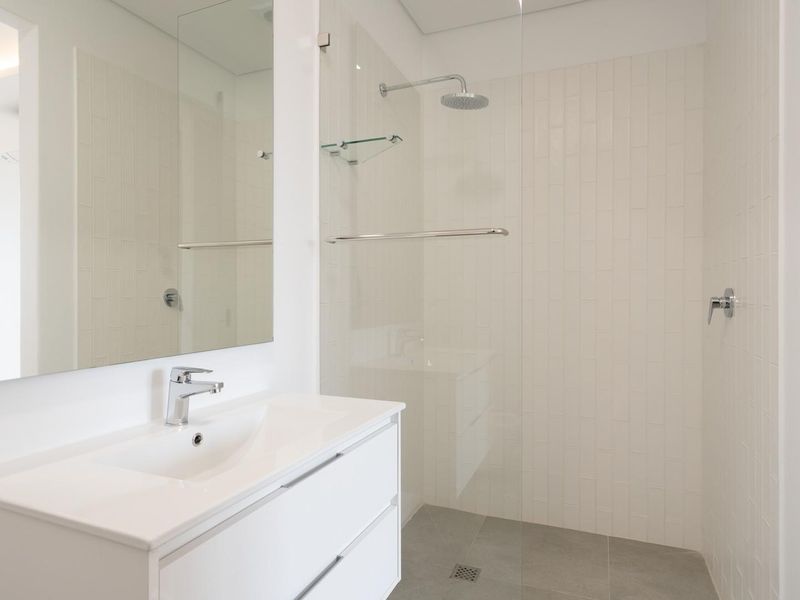 Modern bathroom featuring a sleek vanity with integrated basin, large wall mirror, and a spacious walk-in shower with glass screen and rain shower head.