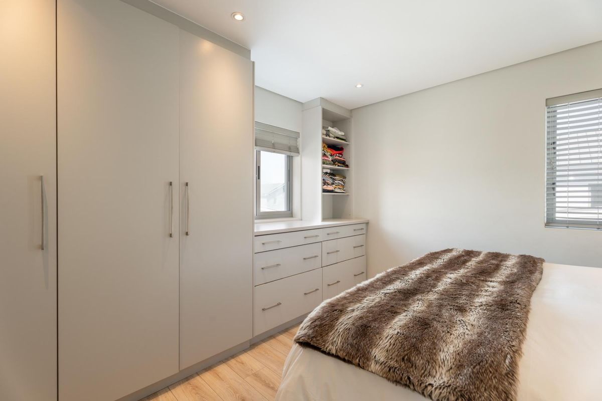 A modern bedroom featuring extensive built-in cabinetry, integrated drawers, recessed lighting, and light-toned laminate flooring with neutral finishes.