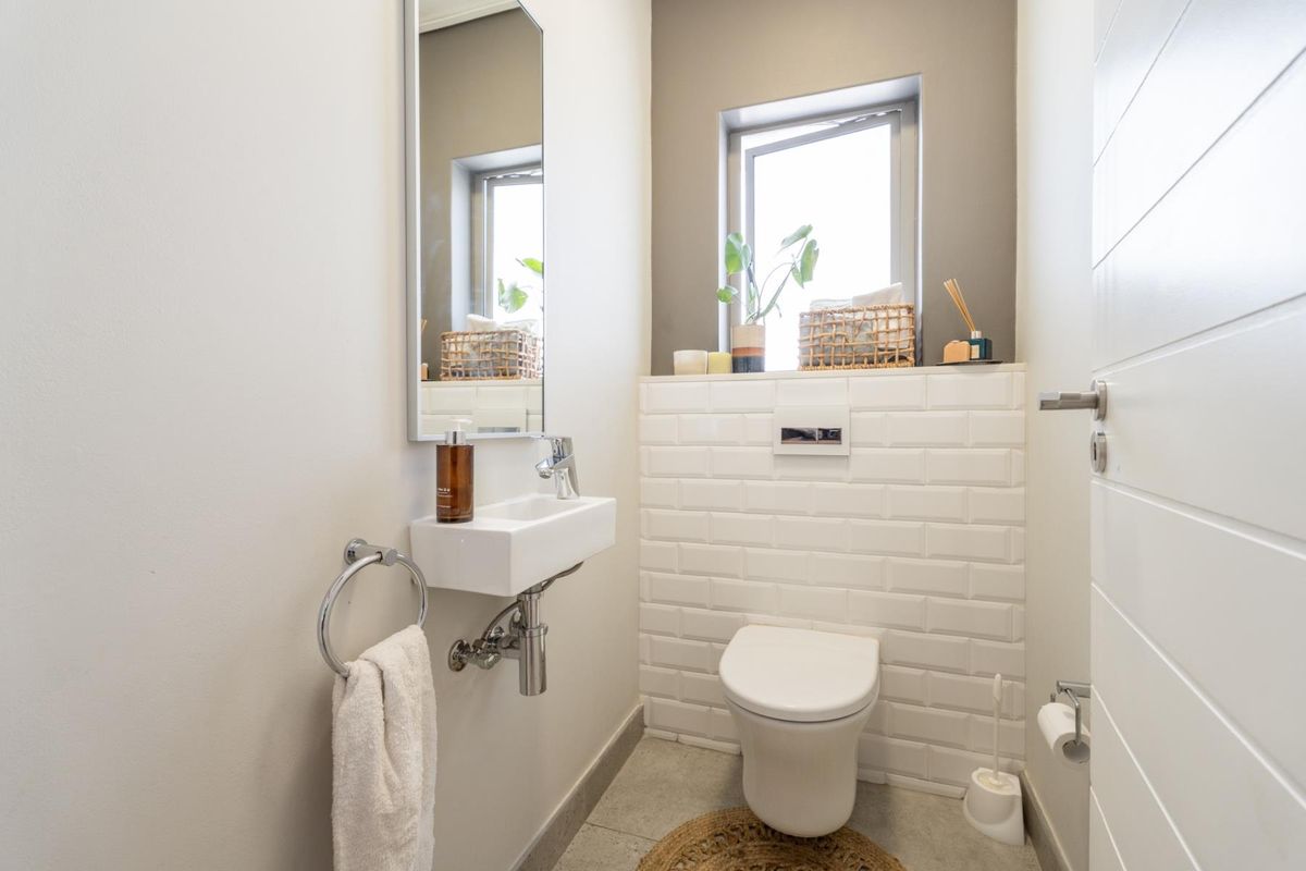 A modern guest cloakroom featuring a wall-mounted toilet with a concealed cistern, subway tile detailing, and a compact wall-mounted basin.