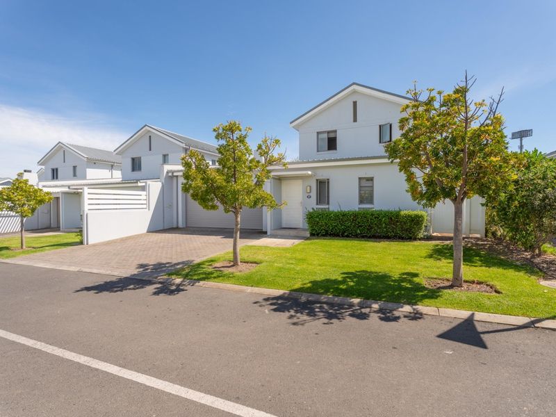 A well-maintained townhouse exterior featuring a paved driveway, integrated garage, and neat front garden with established landscaping.