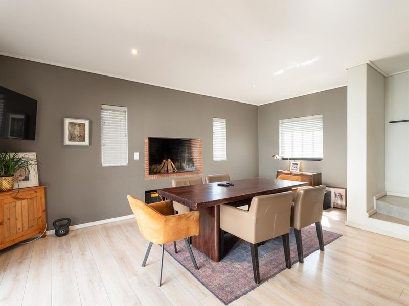 A well-lit dining room featuring laminate flooring, a built-in fireplace with brick detailing, and neutral wall tones, creating a comfortable and functional living space.