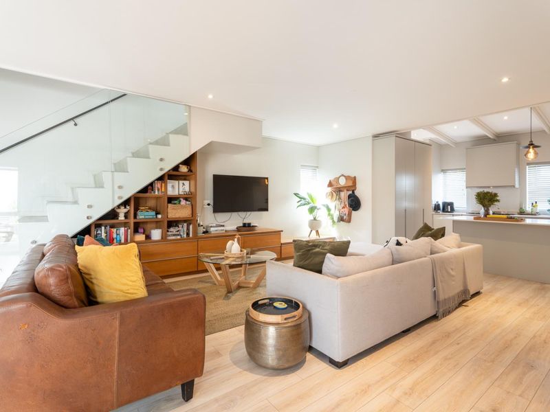 Spacious open-plan living area featuring a modern kitchen with island, light laminate flooring, and a contemporary staircase with glass balustrade.