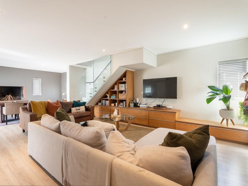 Spacious open-plan living area featuring modern laminate flooring, recessed lighting, a glass balustrade staircase, and custom built-in cabinetry with an integrated fireplace.