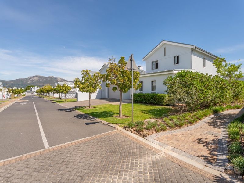 A clear street view of a well-maintained townhouse complex featuring paved driveways, landscaped gardens, and mountain views in the background.