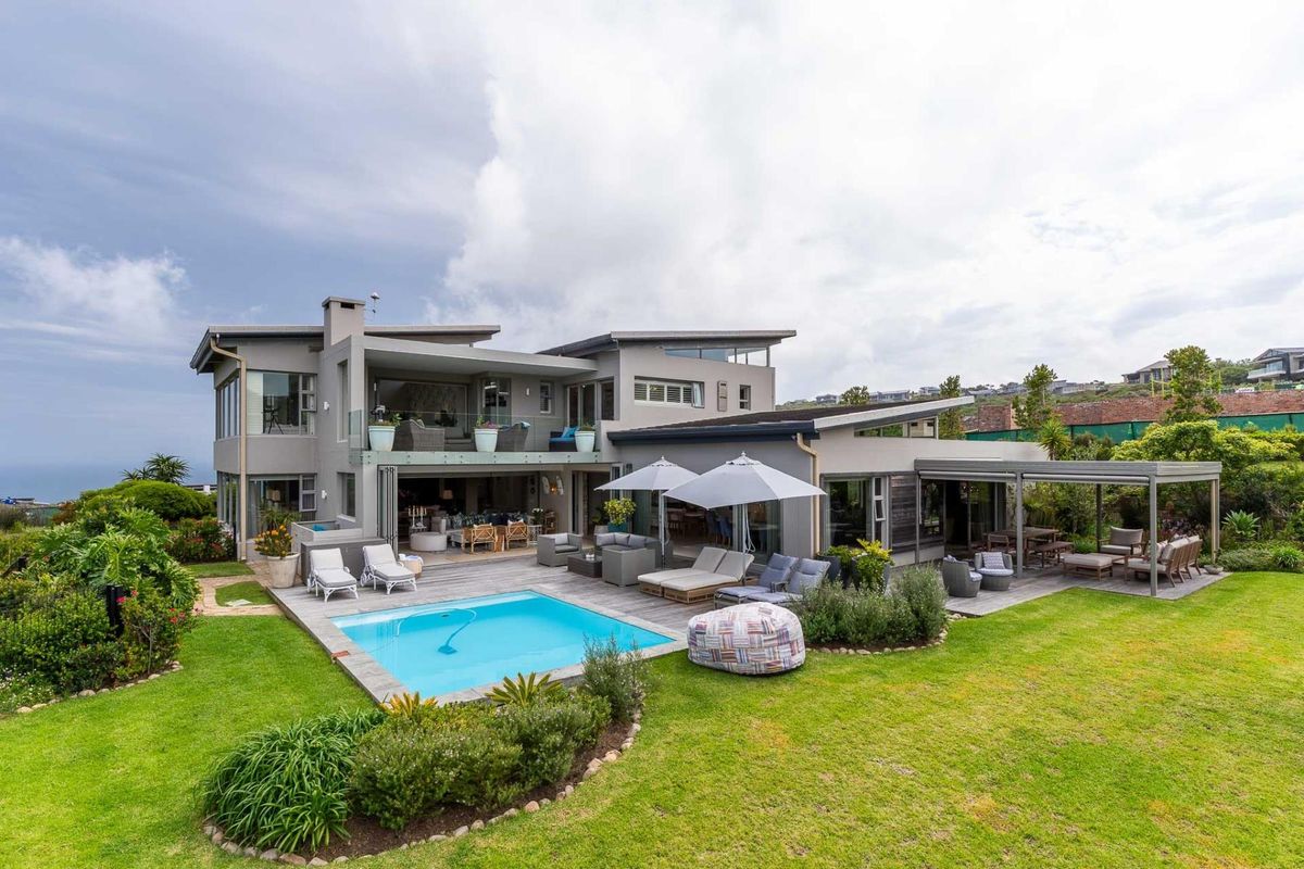 A spacious rear exterior view featuring a modern multi-level home with a swimming pool, timber decking, covered patio, and beautifully landscaped garden.
