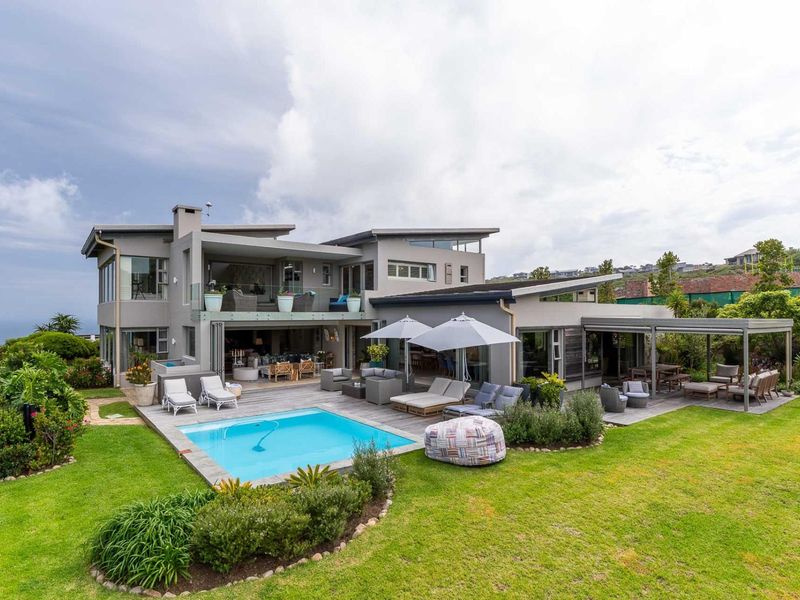 A spacious rear exterior view featuring a modern multi-level home with a swimming pool, timber decking, covered patio, and beautifully landscaped garden.