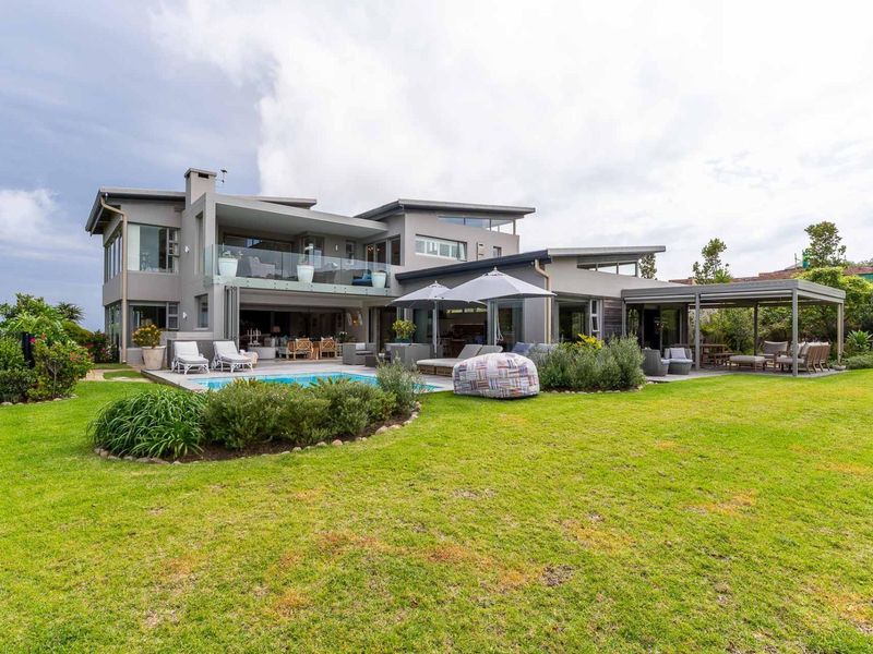 A spacious rear exterior view of a modern multi-level home featuring a swimming pool, covered patio, and well-maintained landscaped garden.