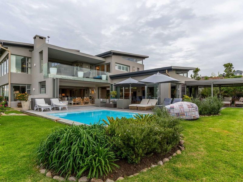 A modern rear exterior view featuring a swimming pool, landscaped garden, covered patio area, and a multi-level architectural design with glass balustrades.
