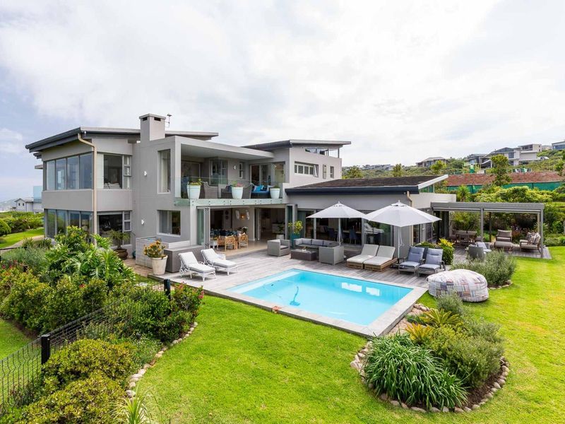 A spacious rear exterior view featuring a modern multi-level home with a swimming pool, timber decking, covered patio, and a well-maintained landscaped garden.