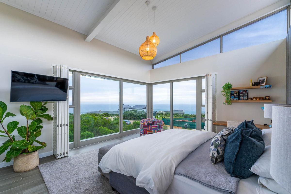 A bright, modern bedroom featuring vaulted ceilings, clerestory windows, and expansive sliding glass doors that offer panoramic coastal views.
