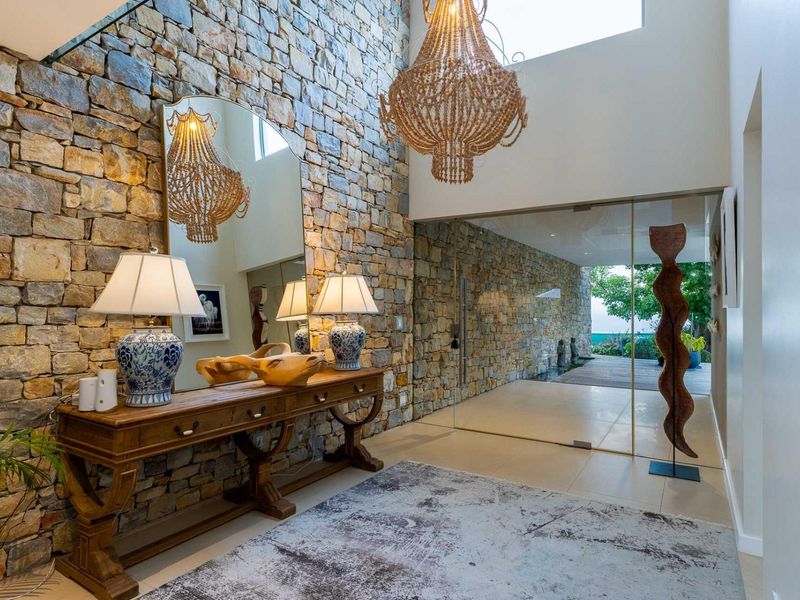 Elegant double-volume entrance hall featuring a striking natural stone feature wall, large format floor tiles, and a seamless glass door leading to the outdoors.