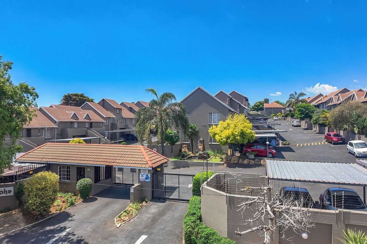 Aerial view of the apartment complex entrance, featuring secure gated access, paved driveways, covered carports, and well-maintained exterior building facades.