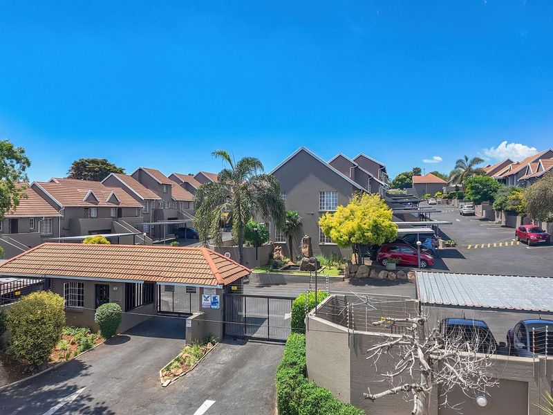 Aerial view of the apartment complex entrance, featuring secure gated access, paved driveways, covered carports, and well-maintained exterior building facades.