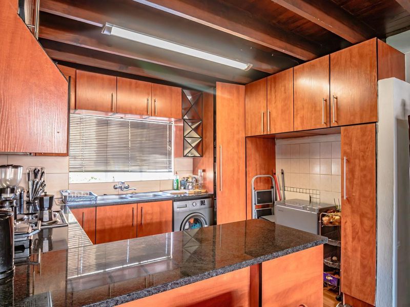 A functional kitchen featuring warm wooden cabinetry, granite countertops, a tiled backsplash, and exposed wooden ceiling beams, with an integrated washing machine.