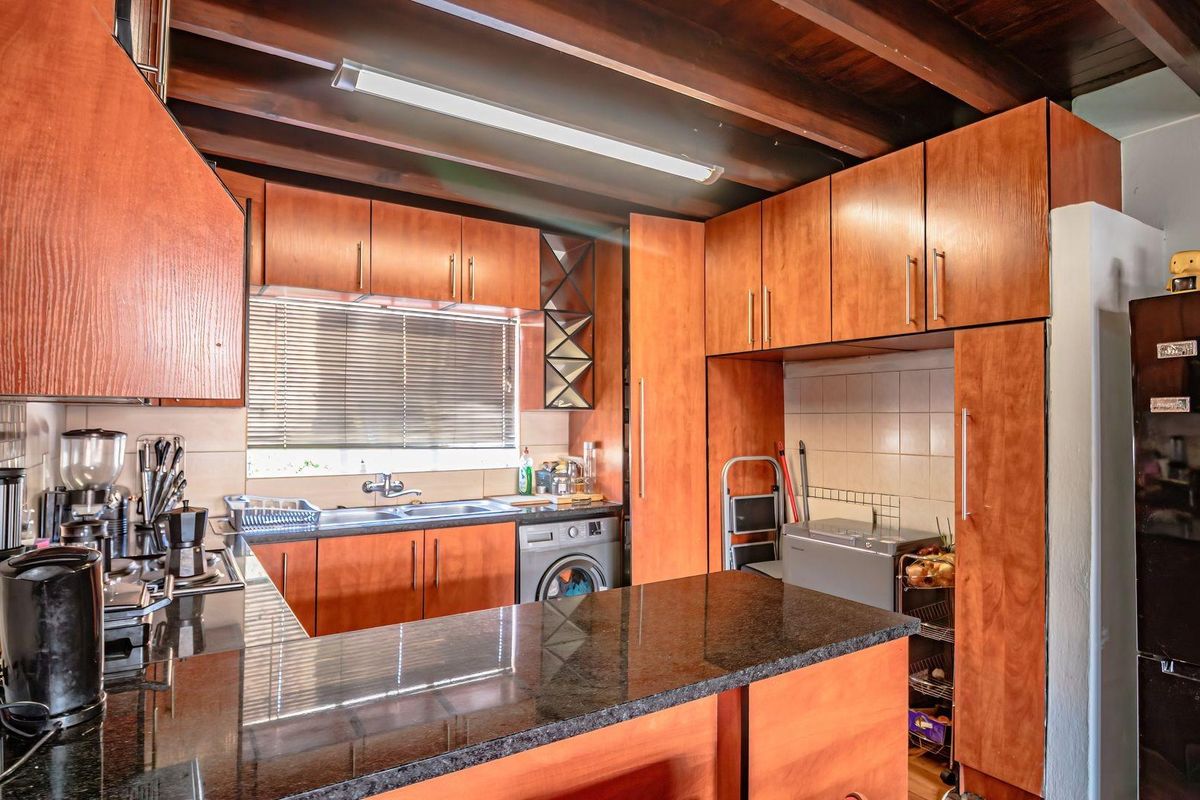 A functional kitchen featuring warm wooden cabinetry, granite countertops, a tiled backsplash, and exposed wooden ceiling beams, with an integrated washing machine.