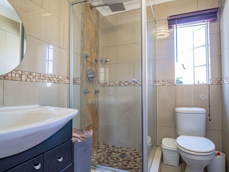 A well-maintained bathroom featuring a modern vanity, a glass-enclosed shower with mosaic tile accents, and a standard toilet.