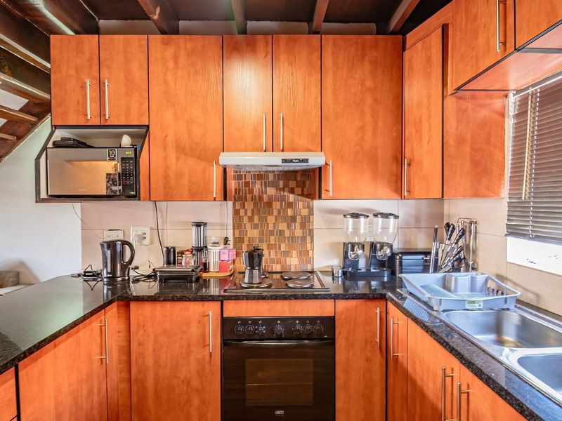 A functional kitchen featuring warm-toned wooden cabinetry, granite countertops, a mosaic tile backsplash, and integrated appliances including an oven and hob.